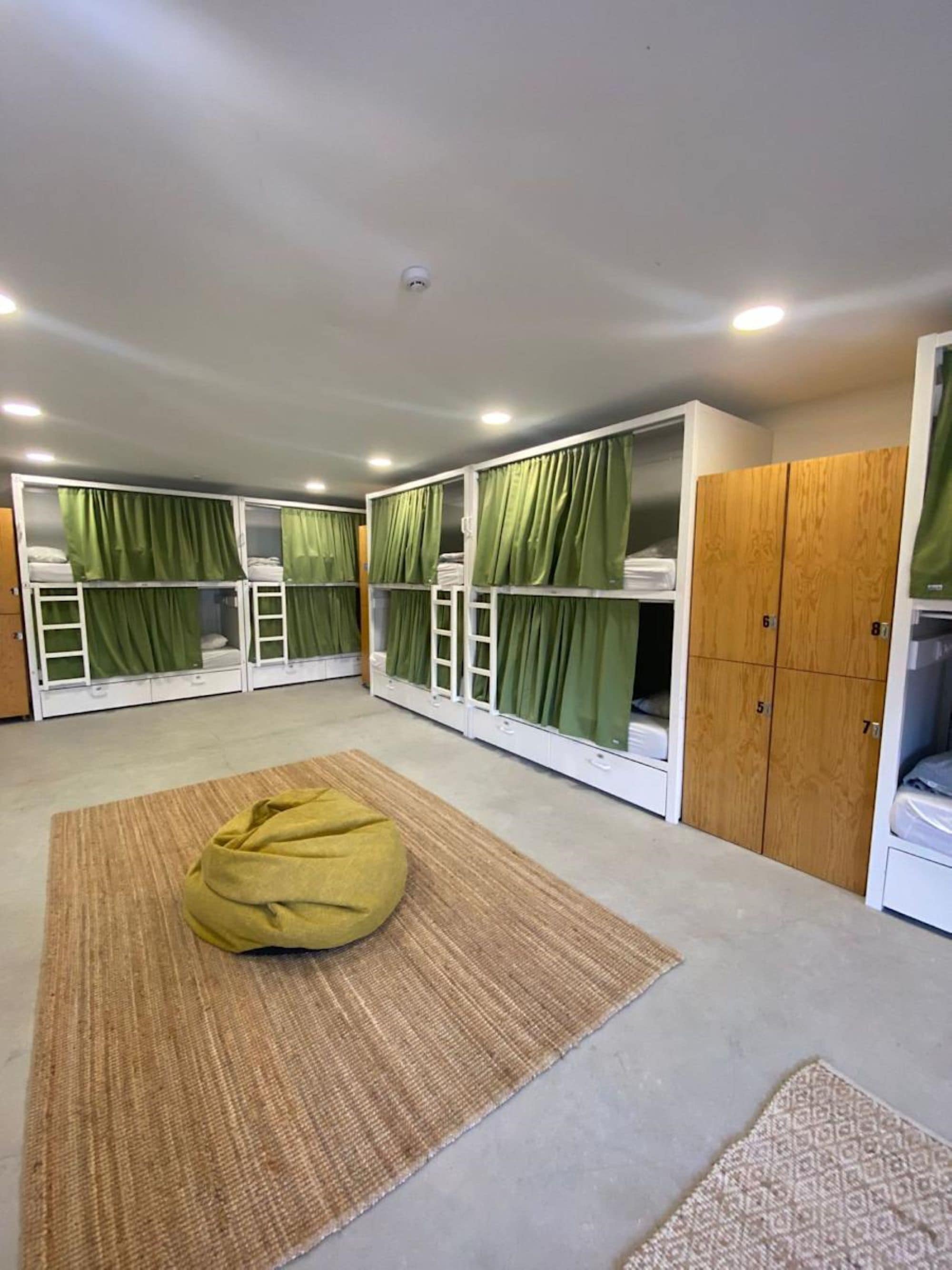 A dormitory room with bunk beds, green curtains, wooden wardrobes, and a bean bag chair.