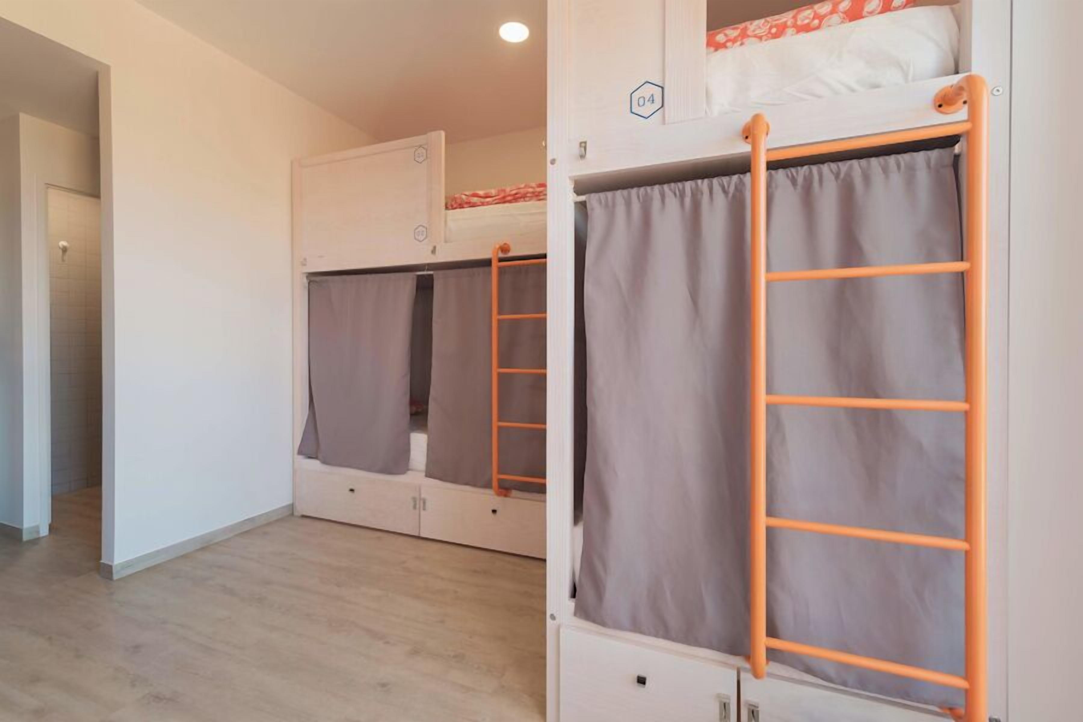 A dormitory room with bunk beds, each with a ladder and a curtain.