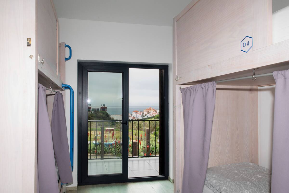 Una habitación con puerta corrediza de vidrio a un balcón, una cama y una mesita.
