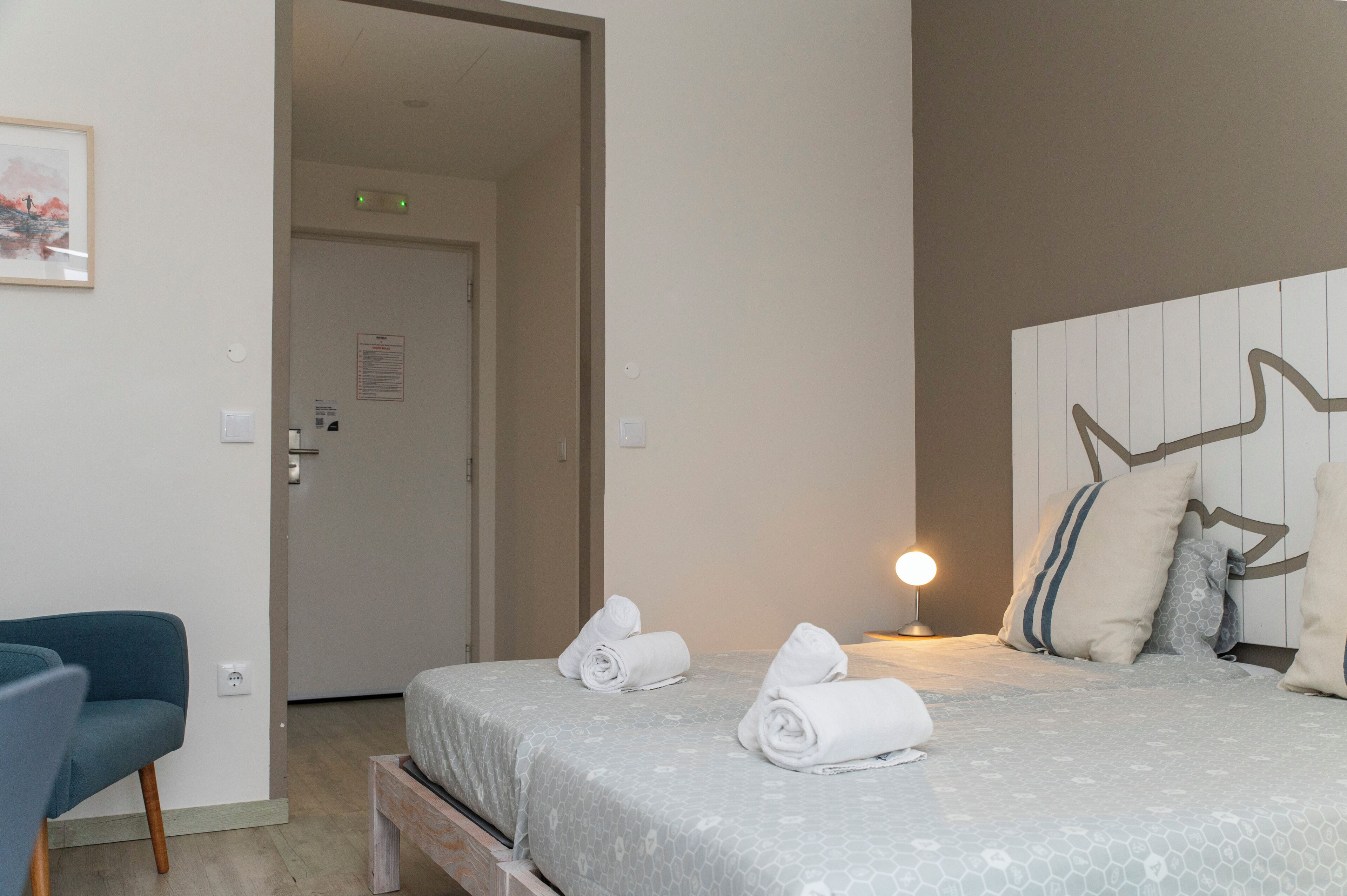 Habitació d'hotel amb un llit, una taula de nit, una cadira i una làmpada penjada a la paret.
