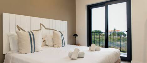 Un dormitorio con una cama grande, cabecera, mesita de noche, lámpara y vistas al exterior a través de una puerta corredera.