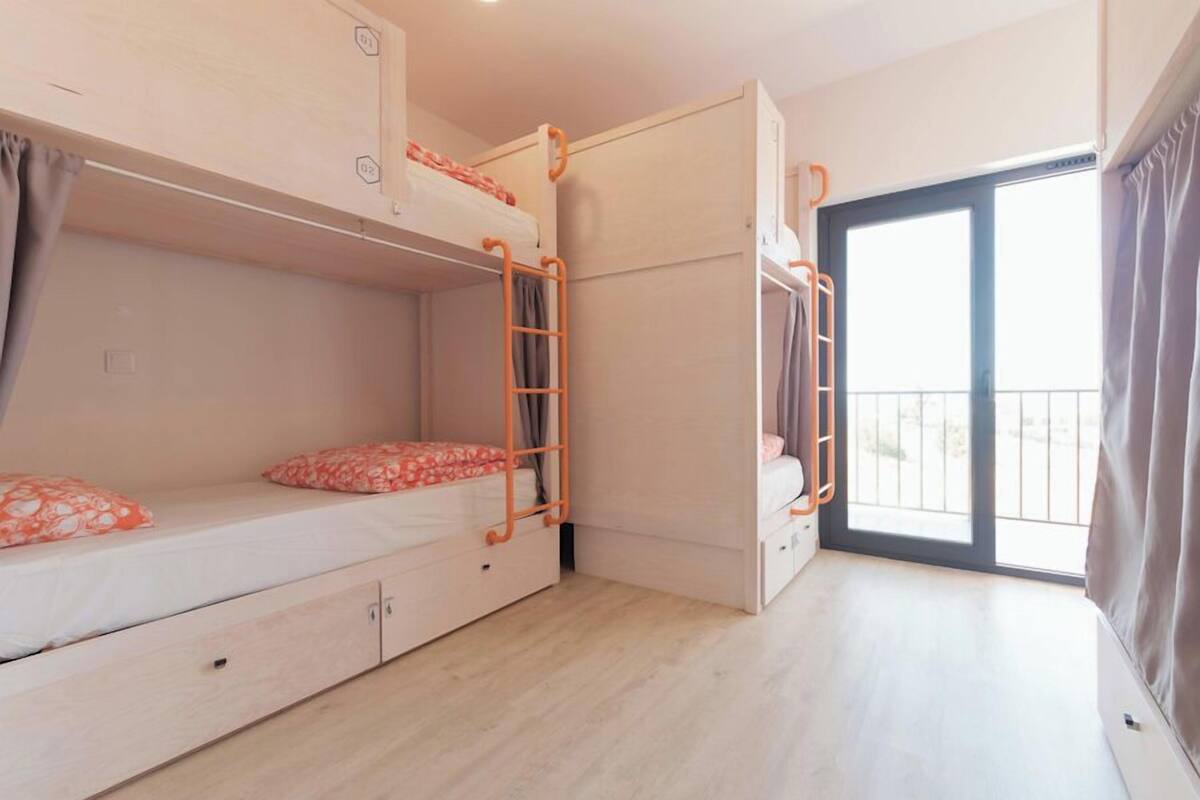 Un dormitorio con literas, una escalera, una ventana y una puerta que da a un balcón.