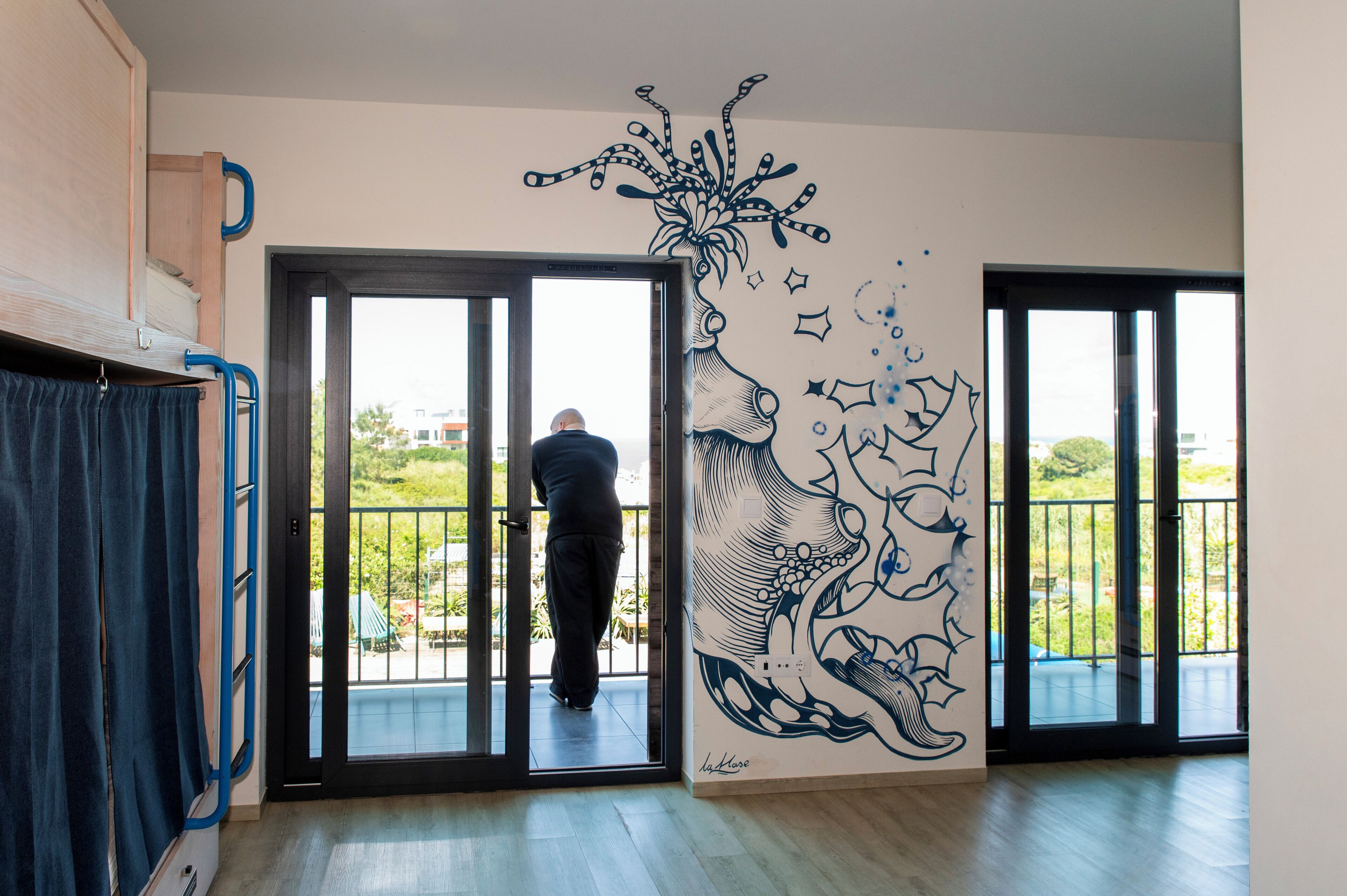 A room with a large window, a balcony, and a wall mural.