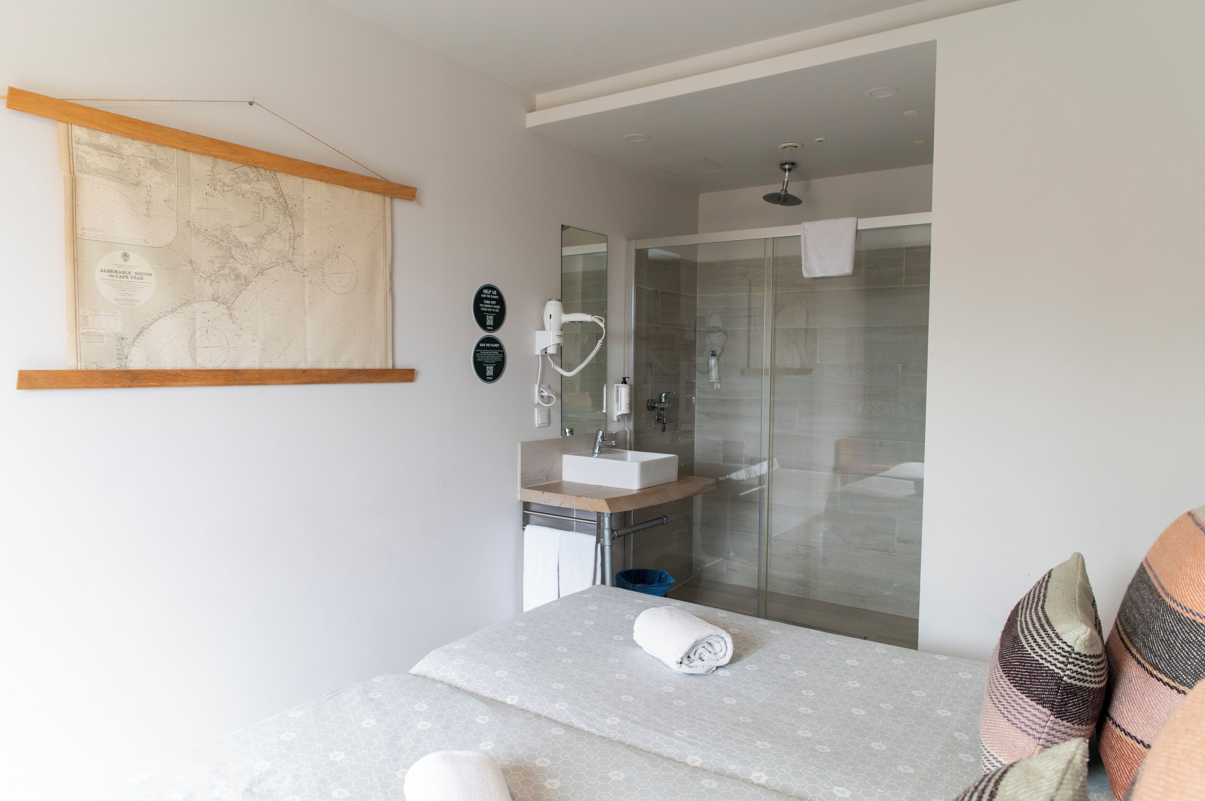 Een moderne hotelkamer met een bed, een badkamer met een douchecabine, een wastafel en een kaart aan de muur.