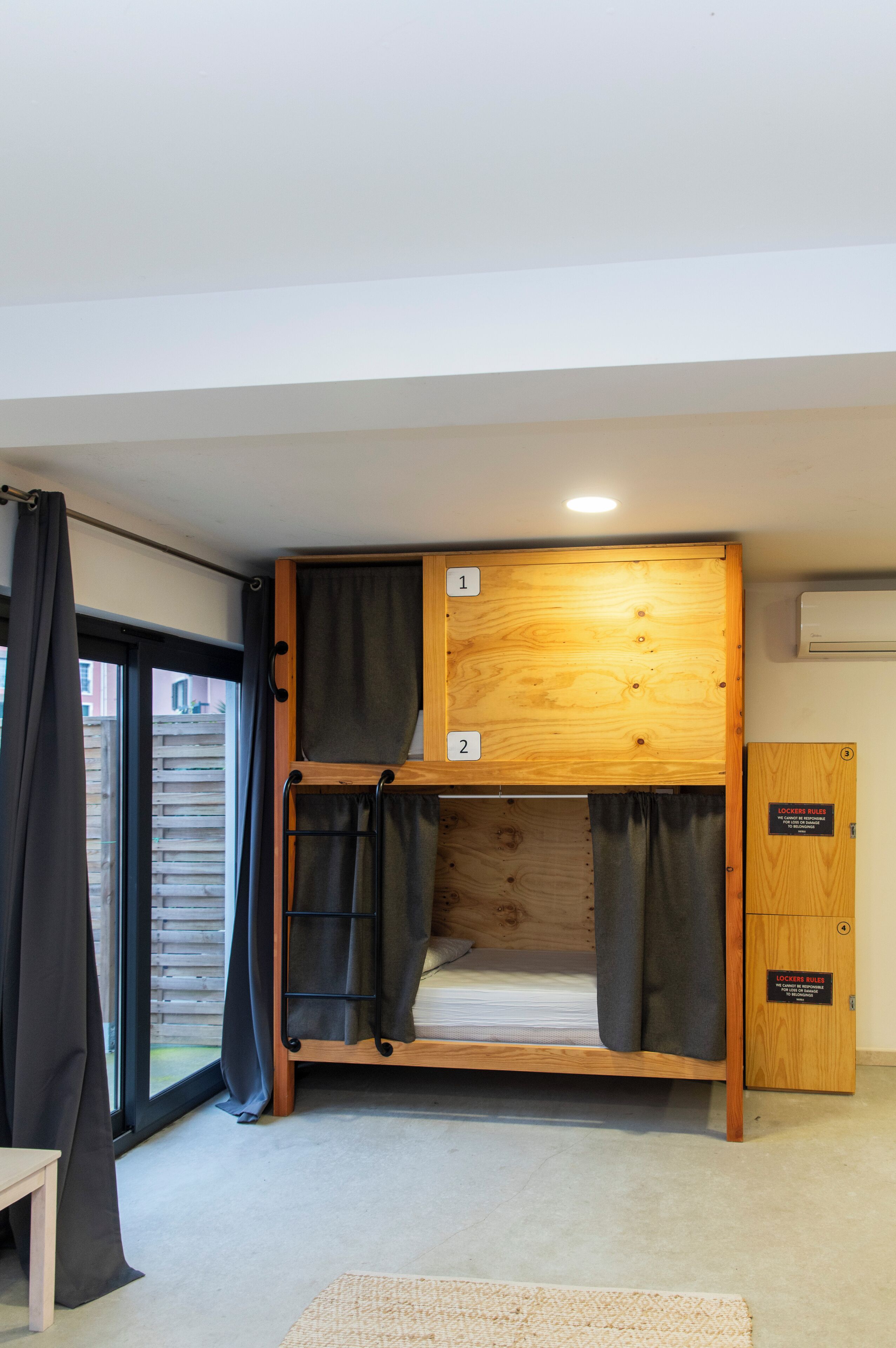 A bunk bed with two levels, each marked with a number. There is a wooden cabinet with a sign, a window with curtains, and a small table.