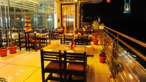 A restaurant with multiple tables and chairs, potted plants, and hanging lanterns. - Hotel Radiant (Kolhapur)