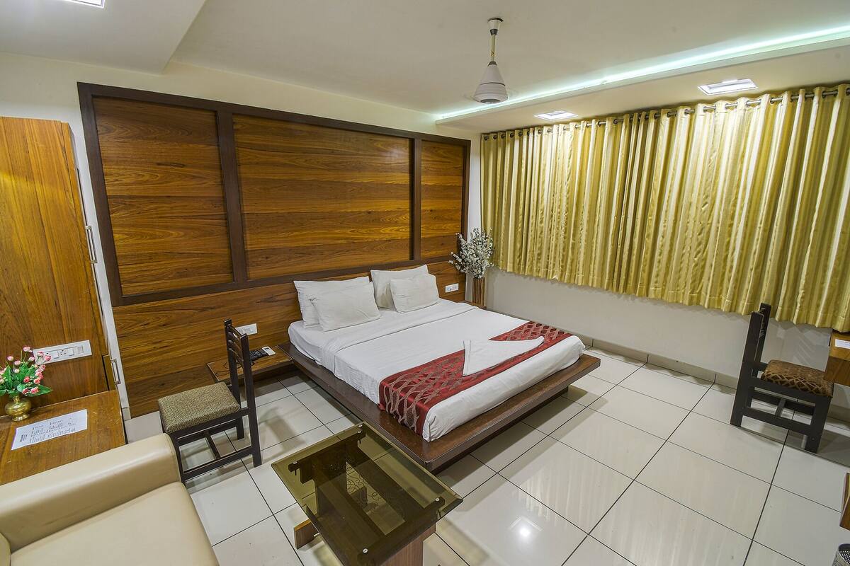A hotel room with a large bed, wooden paneling on the walls, a desk with a chair, and a window with curtains.