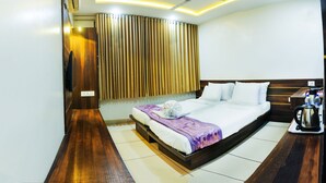 A modern hotel room with a large bed, a flat-screen TV mounted on the wall, a ceiling fan, and a coffee maker on the side table. - Hotel Radiant (Kolhapur)