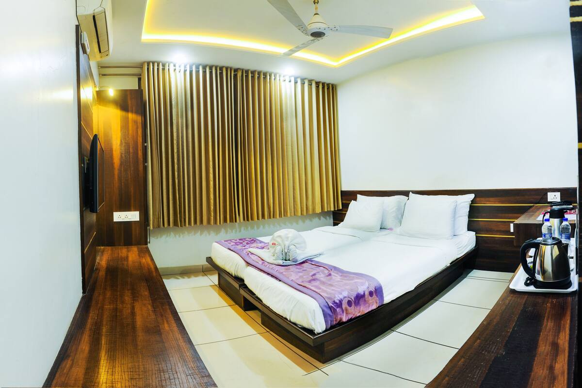 A modern hotel room with a large bed, a flat-screen TV mounted on the wall, a ceiling fan, and a coffee maker on the side table.