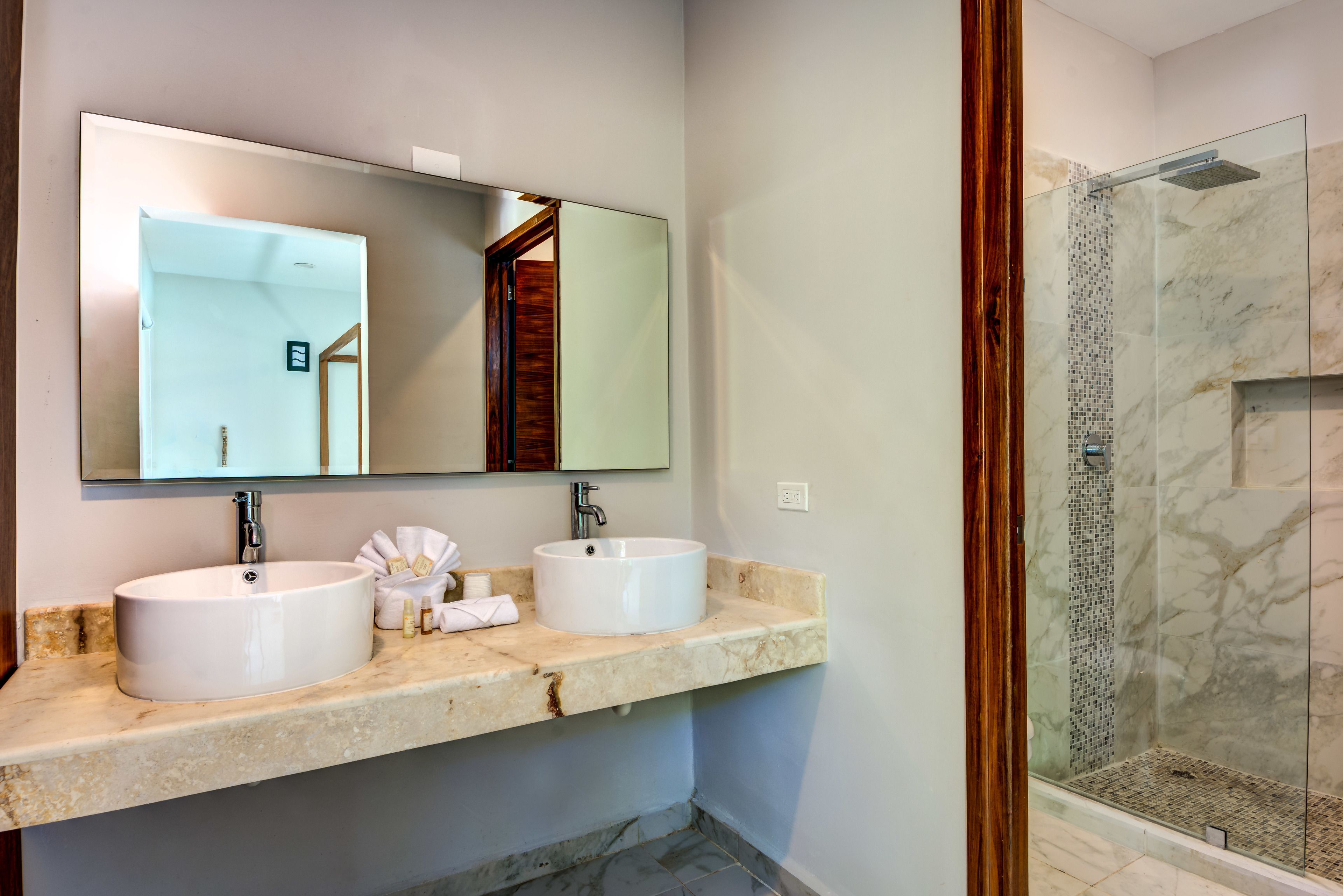 Un baño con dos lavamanos, un espejo grande y una cabina de ducha con paredes de vidrio.