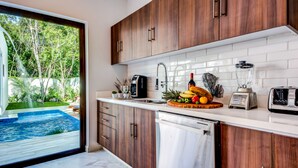 A modern kitchen with wooden cabinets, a white countertop, and a view of a swimming pool and greenery outside.