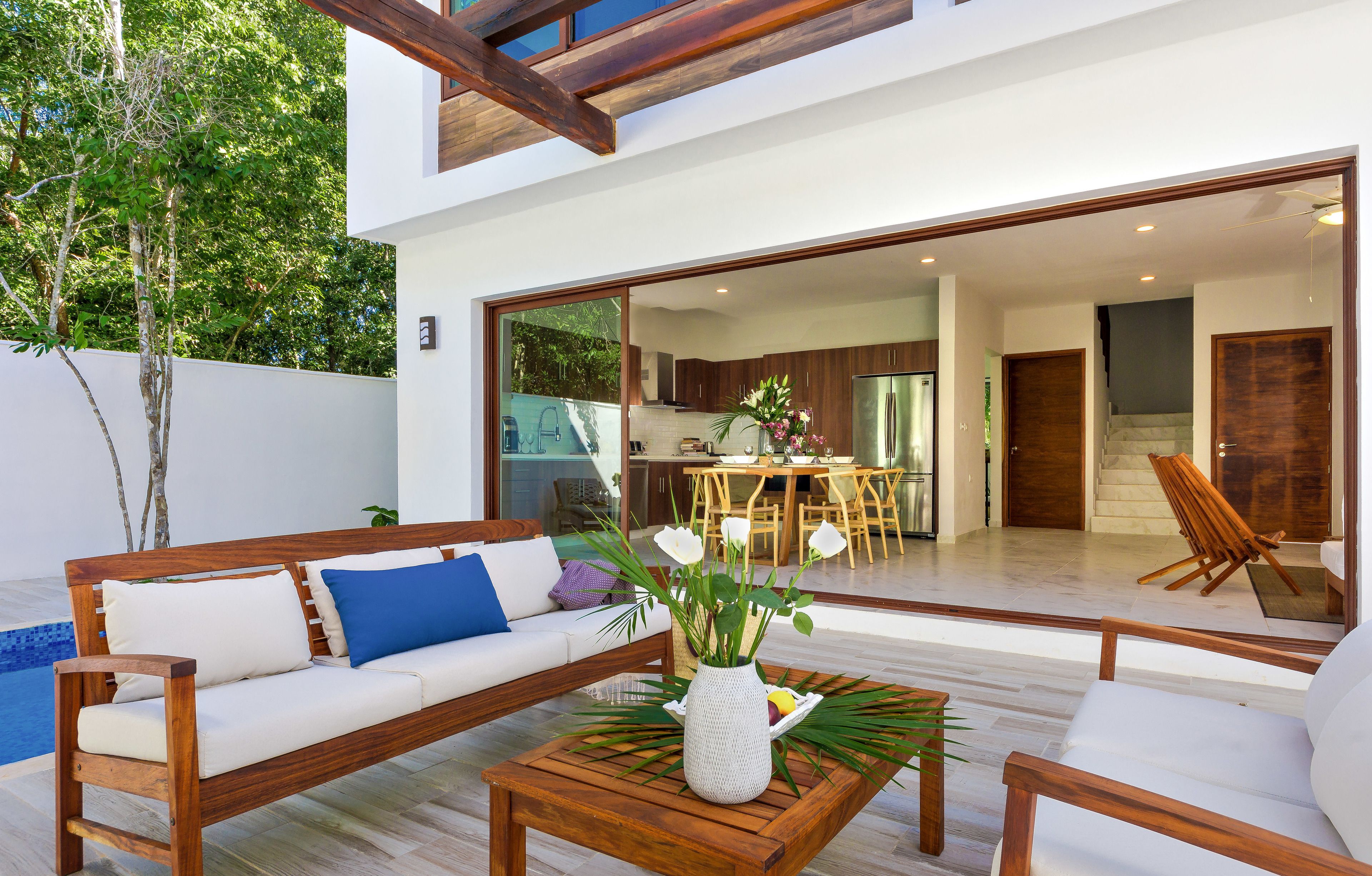 A modern outdoor living area with a wooden bench, a white sofa with blue cushions, and a coffee table with a vase of flowers.
