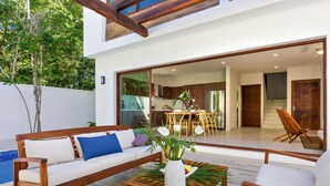 A modern outdoor living area with a wooden bench, a white sofa with blue cushions, and a coffee table with a vase of flowers.