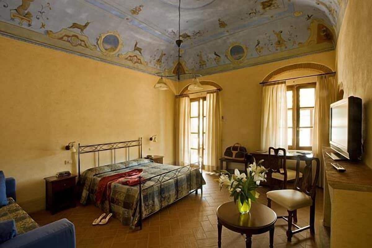 A room with a bed, a desk, a chair, a television, and a ceiling with frescoes.