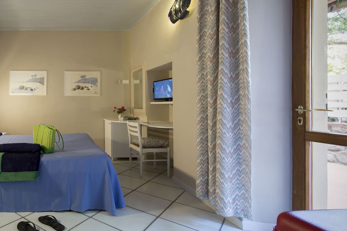 A bedroom with two beds, a desk, a television, and a window with curtains.
