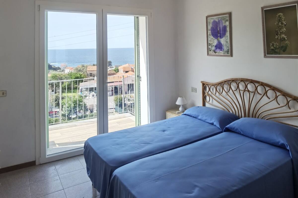 A room with two beds, a balcony with a view of the sea, and two framed artworks on the wall.