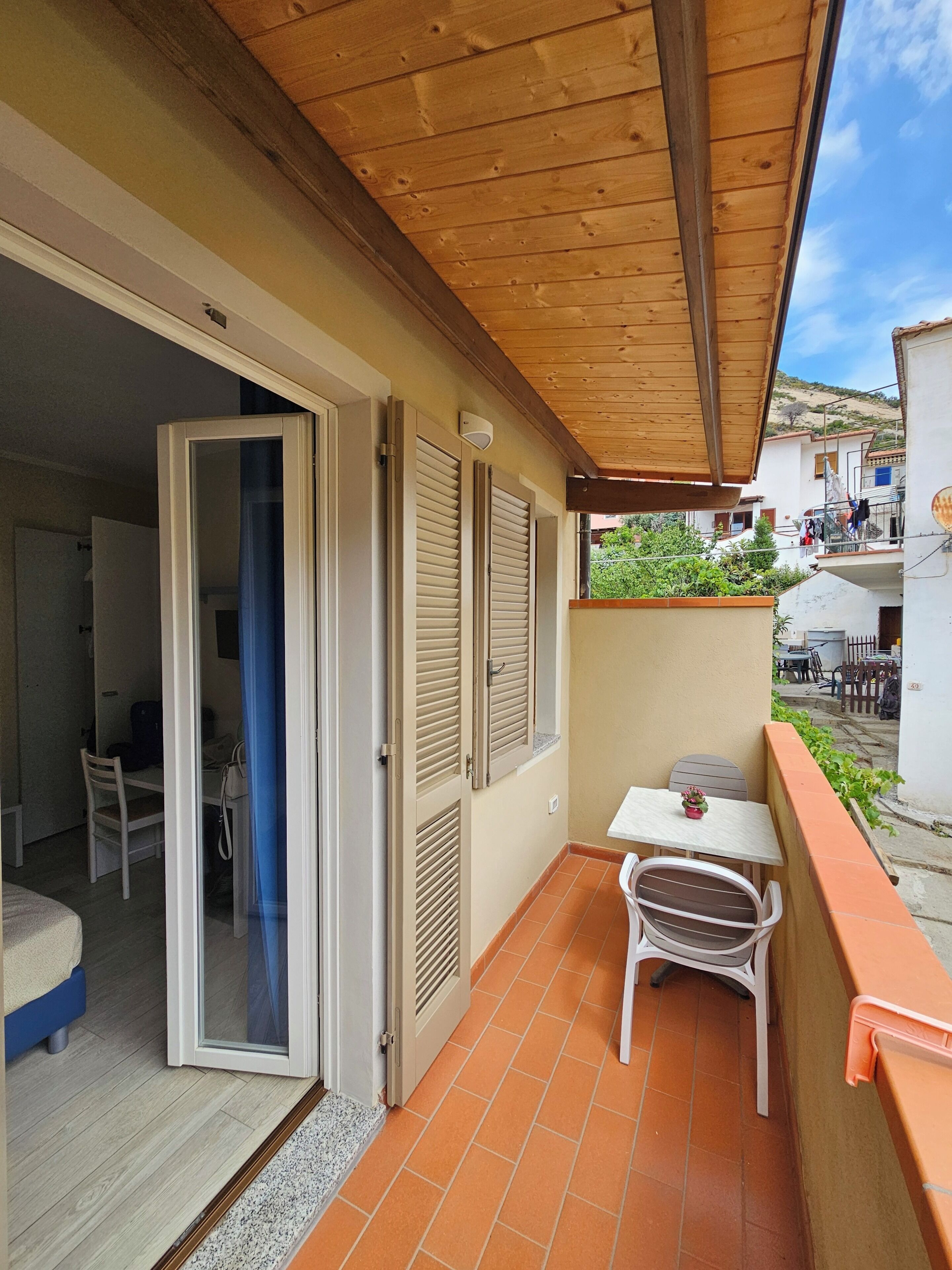 A balcony with a wooden ceiling, a table with chairs, and a door leading to an interior room.