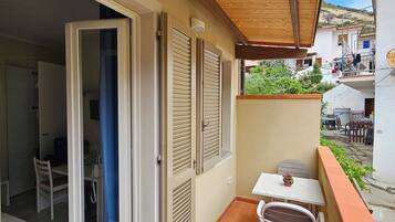 A balcony with a wooden ceiling, a table with chairs, and a door leading to an interior room.