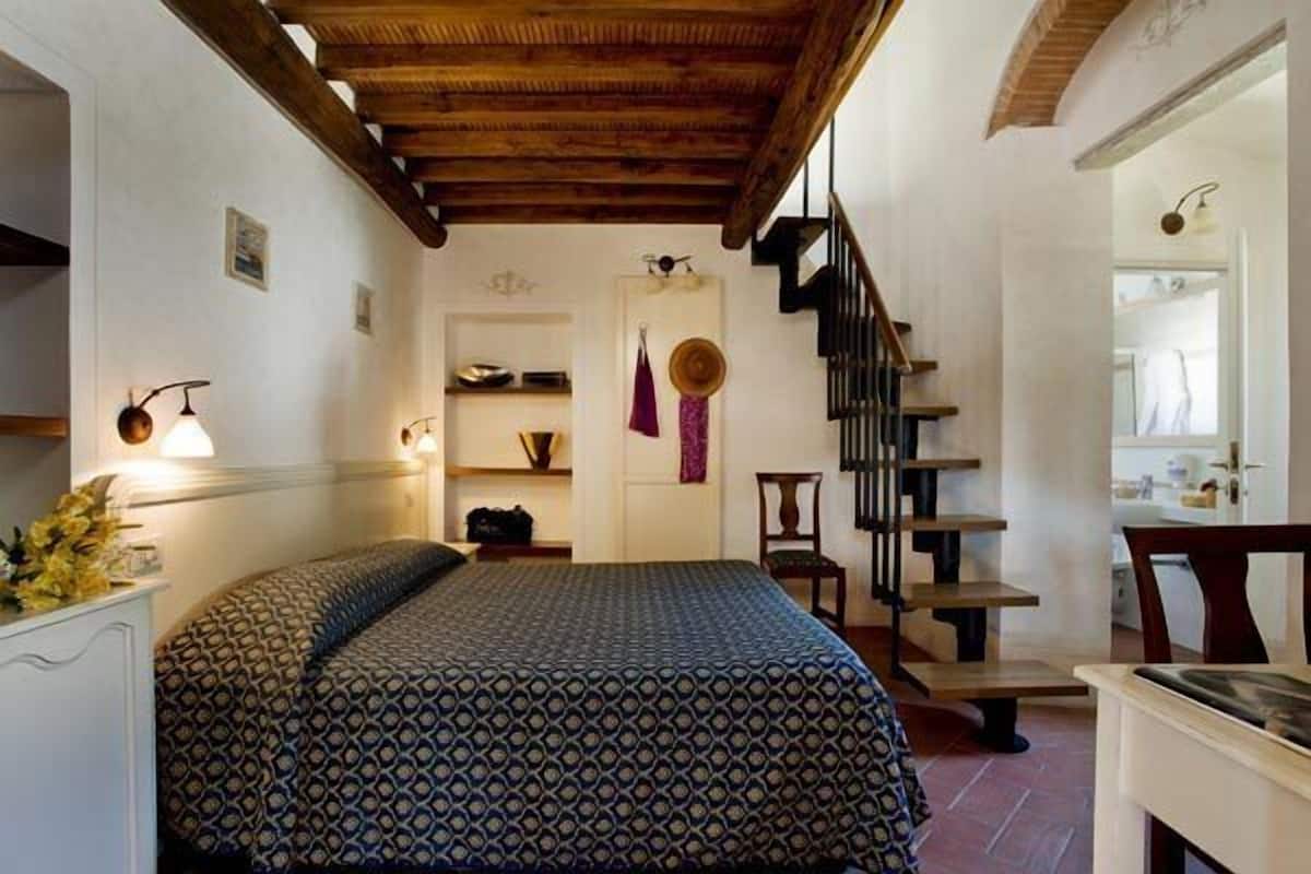A bedroom with a patterned bedspread, a wooden staircase, and a small desk with a chair.