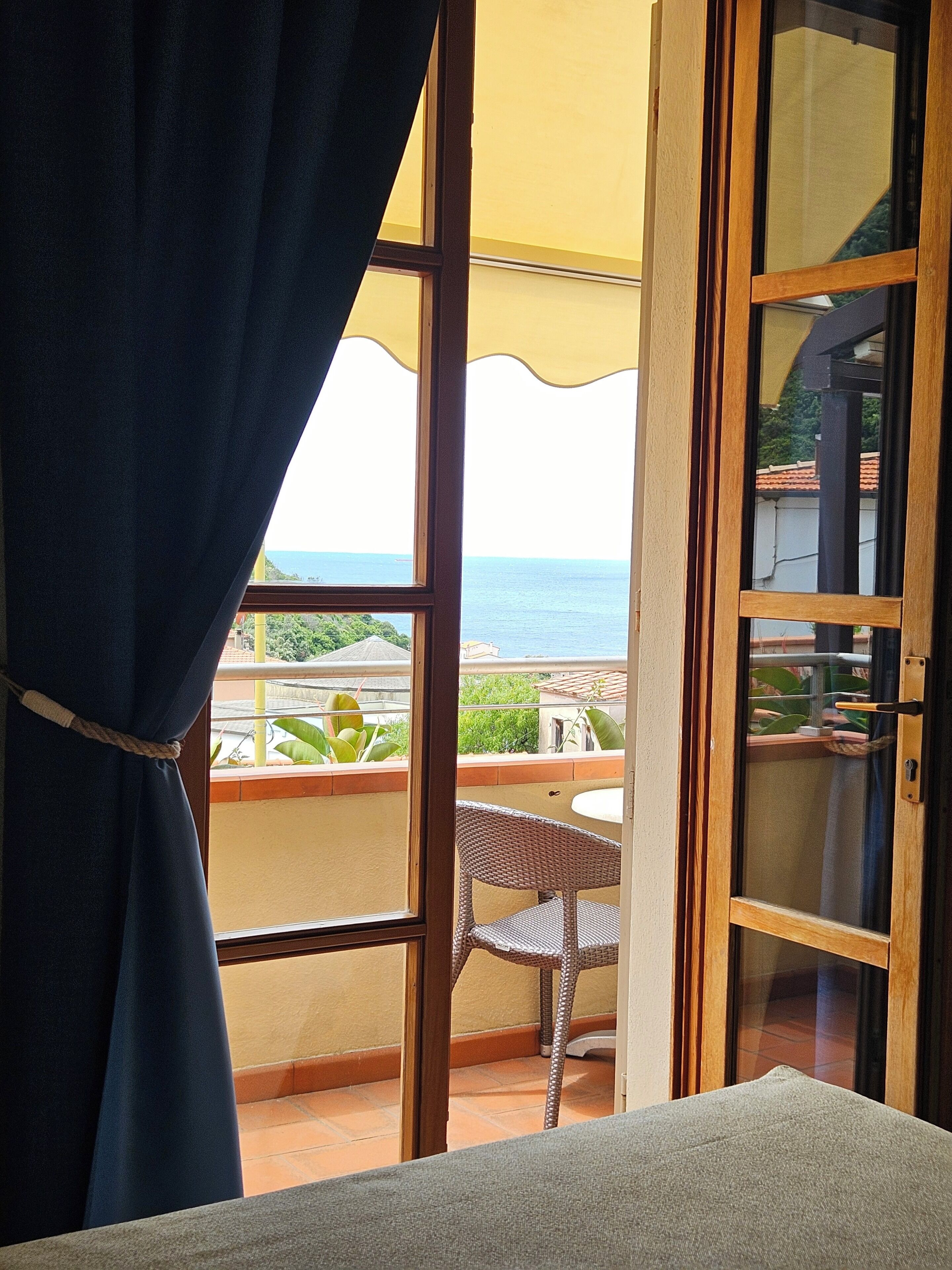 Une pièce avec vue sur la mer, grâce à une grande fenêtre, comprenant un fauteuil en osier et un rideau.