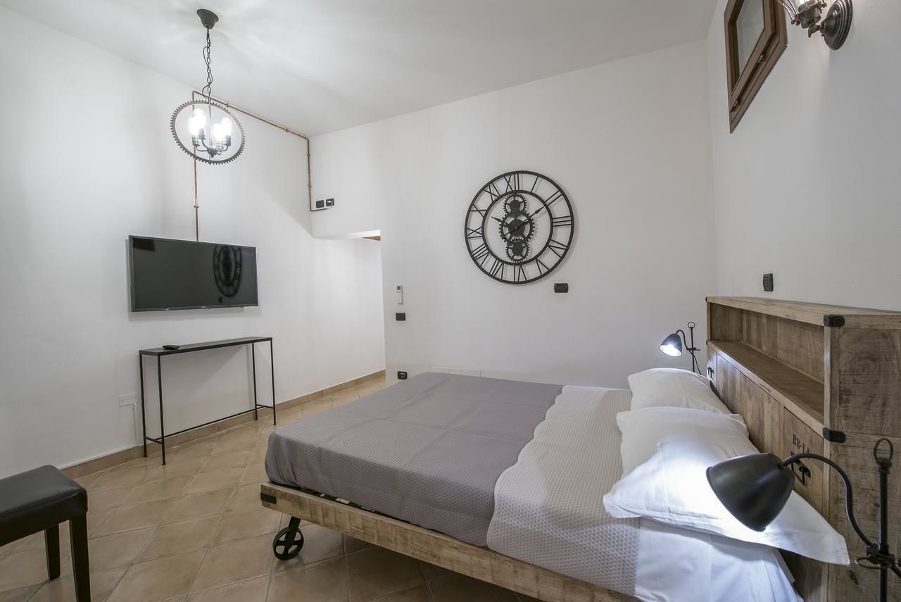 A bedroom with a bed, a TV on a stand, a wall clock, and a wooden headboard.