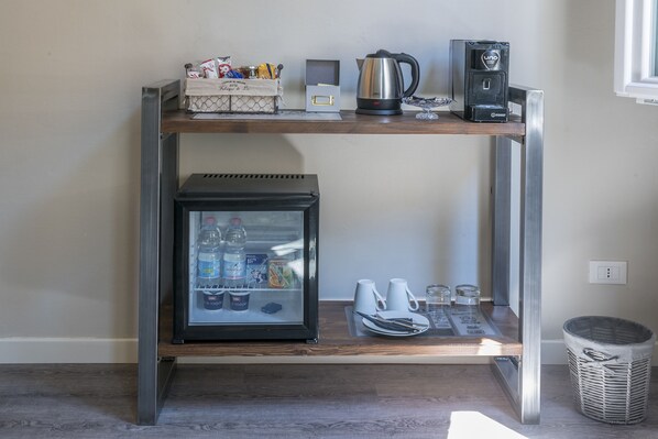 Una kitchenette compacta con un refrigerador, una cafetera y un hervidor sobre una estante.