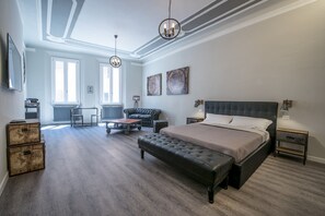 A spacious bedroom with a large bed, a leather sofa, and a dining table. There are two windows providing natural light, and the room features a modern ceiling design. - Steam House - Room & Breakfast (Bologna)