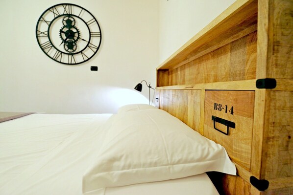 A bed with white bedding, a wooden headboard with a label, and a wall-mounted clock. - Steam House - Room & Breakfast (Bologna)