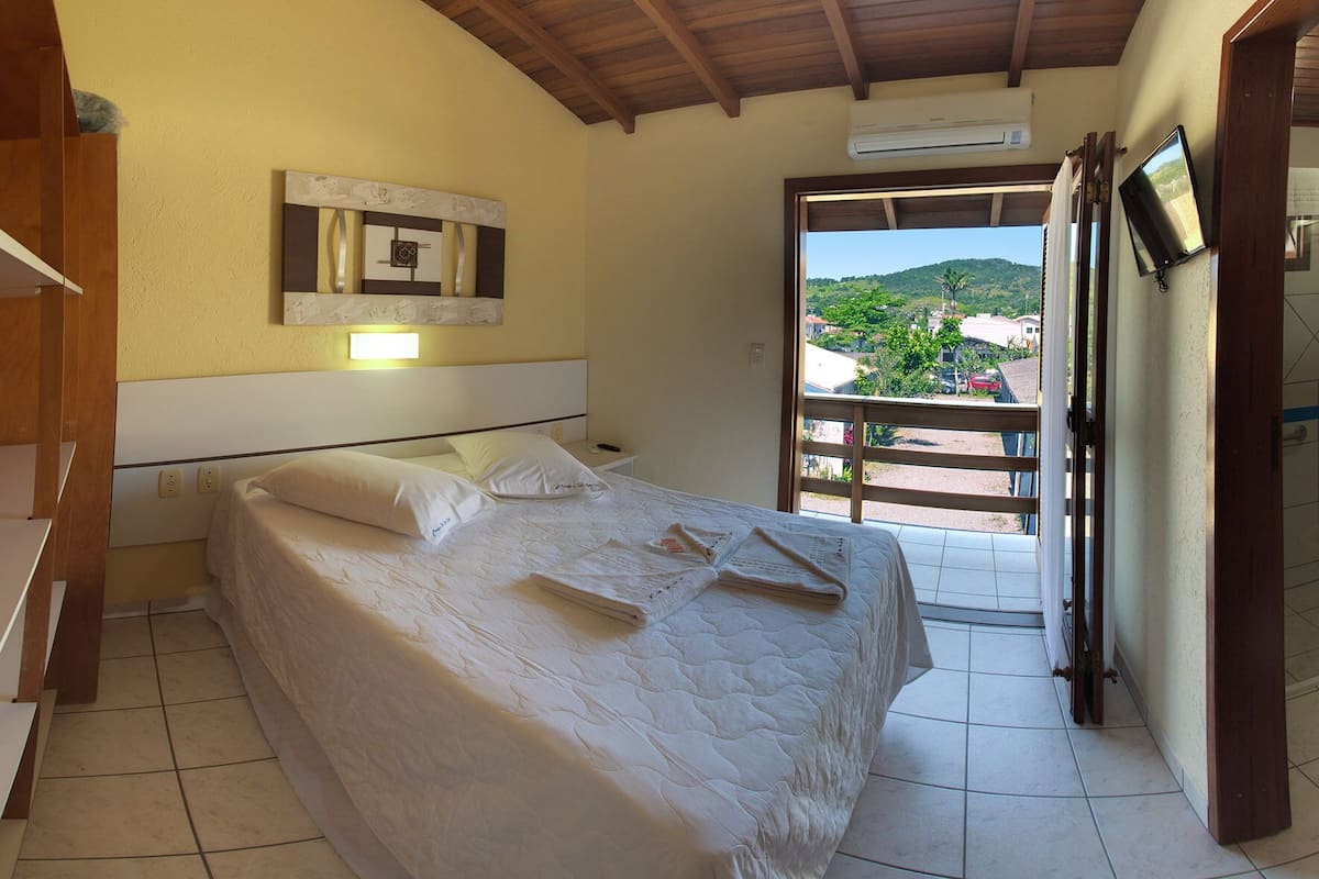 A bedroom with a bed, a nightstand, a wall-mounted TV, and a view of a balcony with a door.