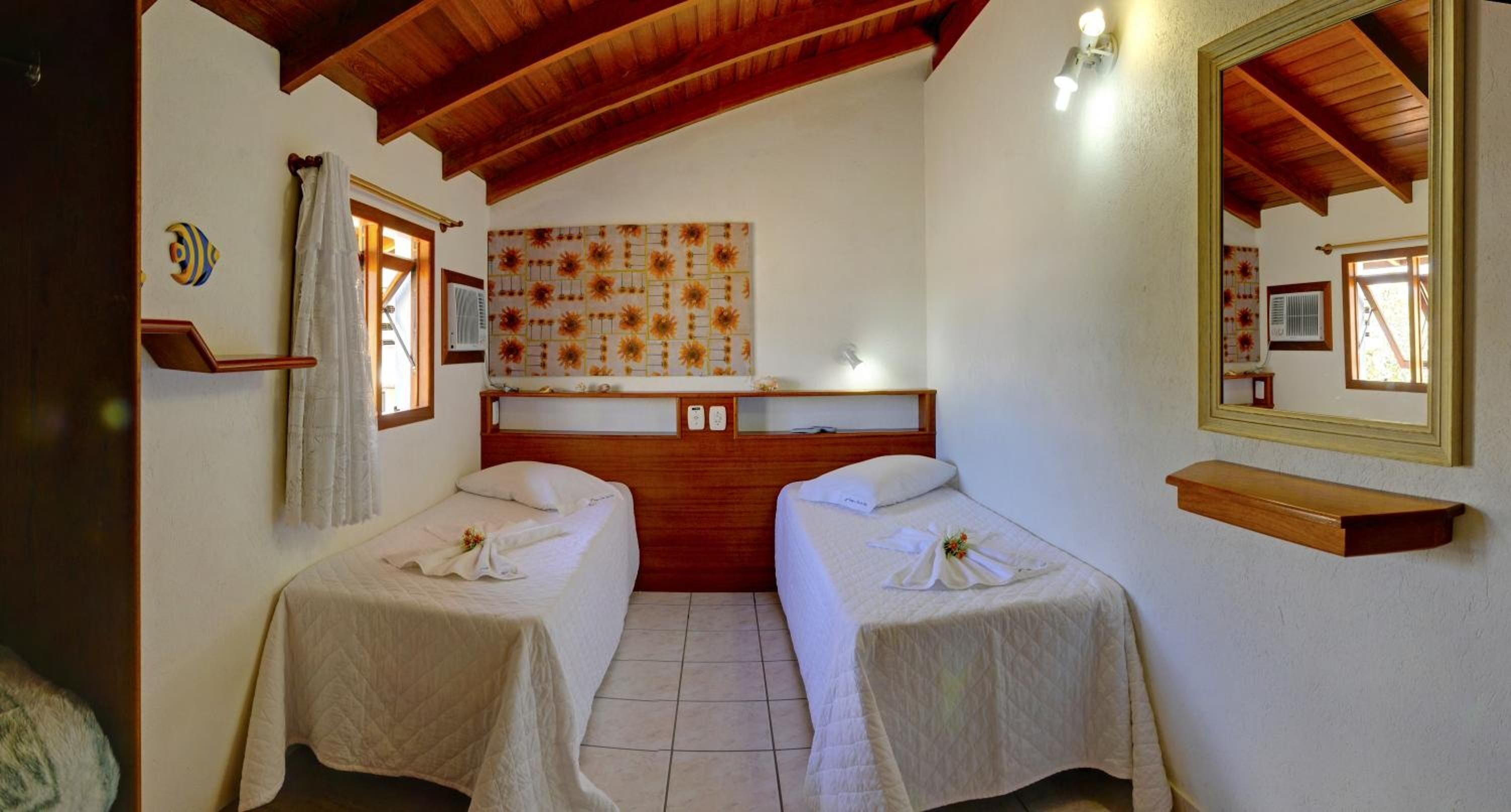 Une chambre avec deux lits, des poutres en bois au plafond, un miroir fixé au mur et une œuvre d’art ornée de motifs de tournesols.