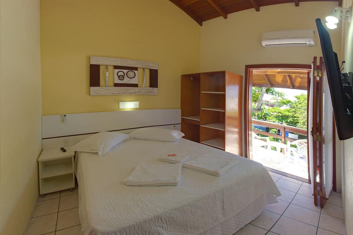 A bedroom with a bed, a nightstand, a wooden wardrobe, a mirror, and a view of the outside.