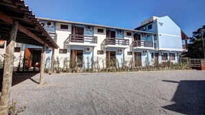 A multi-story building with balconies, a gravel driveway, and a clear blue sky. - Morada do Sol Apart Hotel Garopaba (Garopaba)