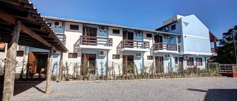 A multi-story building with balconies, a gravel driveway, and a clear blue sky.