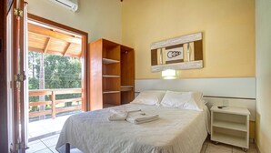 A bedroom with a bed, a nightstand, a shelf unit, and a sliding door leading to a balcony. - Morada do Sol Apart Hotel Garopaba (Garopaba)