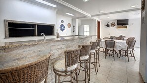 A dining area with wicker chairs, a marble counter, and a television mounted on the wall. - Morada do Sol Apart Hotel Garopaba (Garopaba)