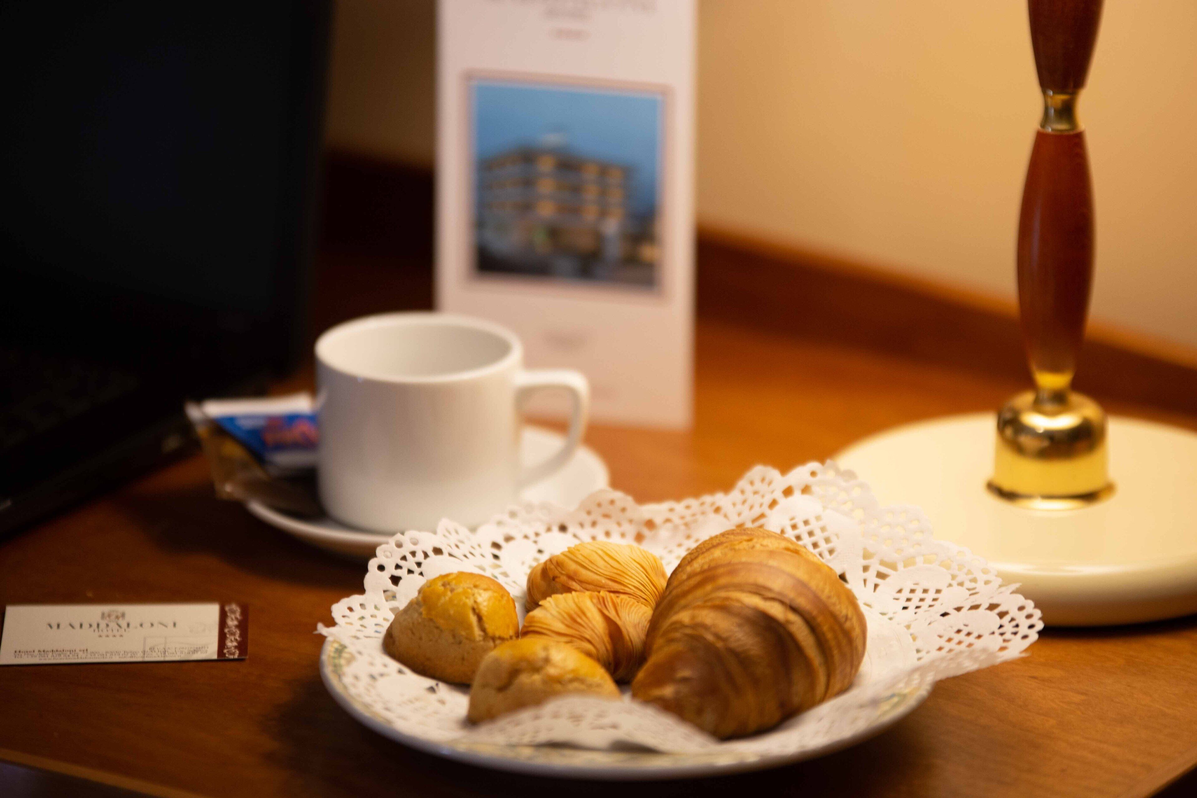 A plate of croissants on a white doily, a white cup, and a small sign with a picture of a building.