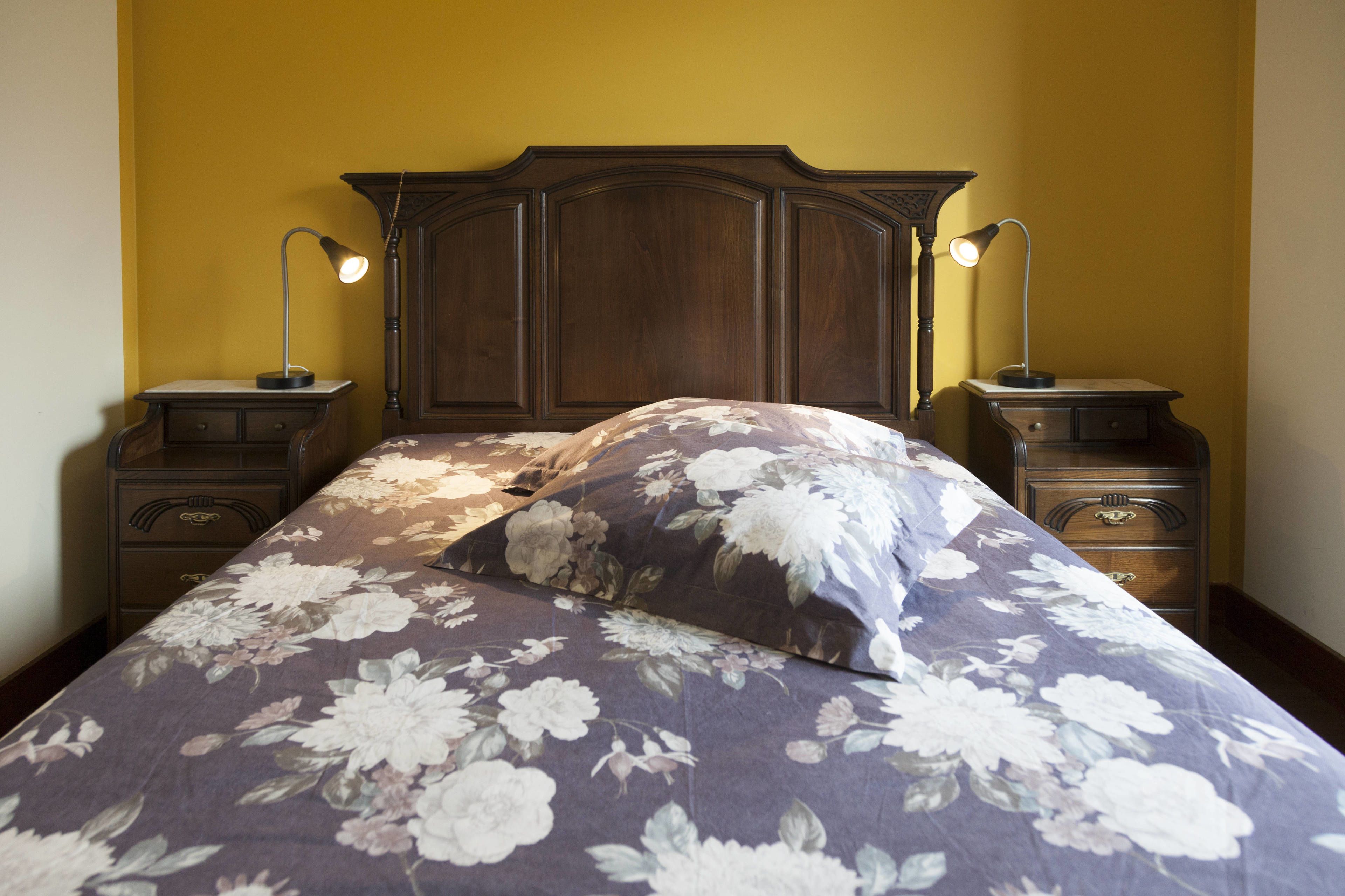 A bedroom with a floral bedspread, wooden headboard, two bedside tables with lamps, and a nightstand with drawers.