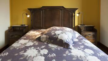 A bedroom with a floral bedspread, wooden headboard, two bedside tables with lamps, and a nightstand with drawers.