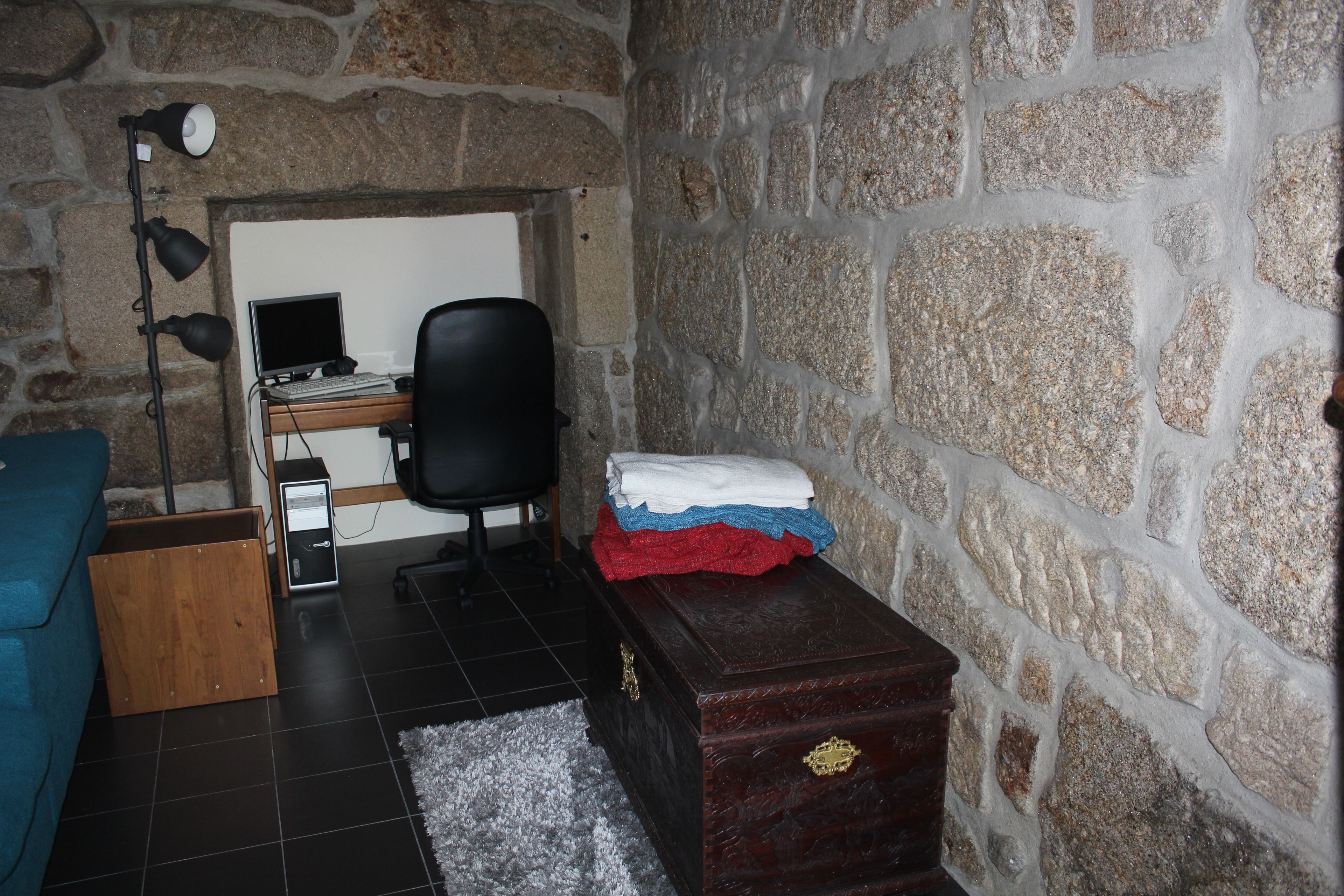 A room with a stone wall, a desk with a computer, a chair, a wooden cabinet, and a blue sofa.