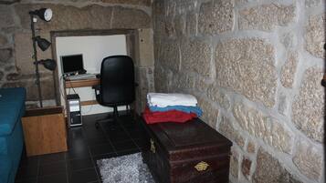A room with a stone wall, a desk with a computer, a chair, a wooden cabinet, and a blue sofa.