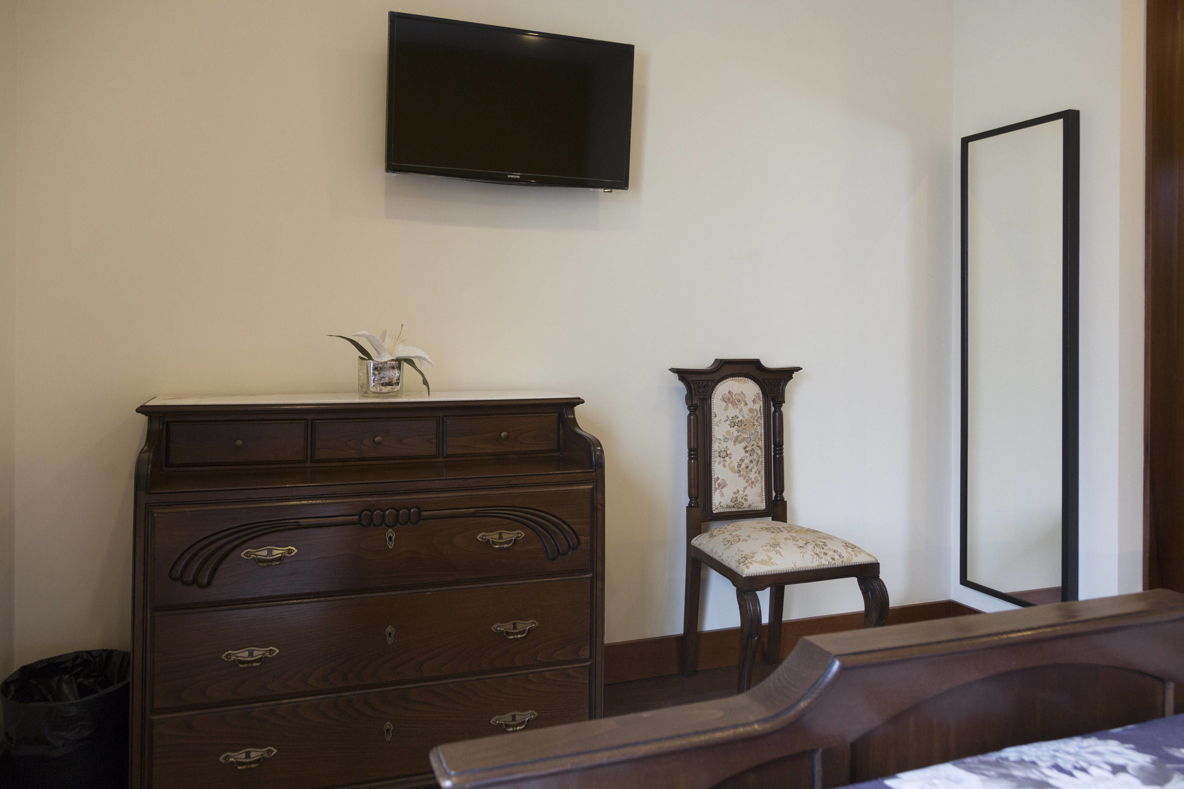 Un dormitorio con un aparador de madera, una silla, un televisor montado en la pared y un espejo grande.