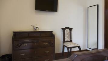 Un dormitorio con un aparador de madera, una silla, un televisor montado en la pared y un espejo grande.