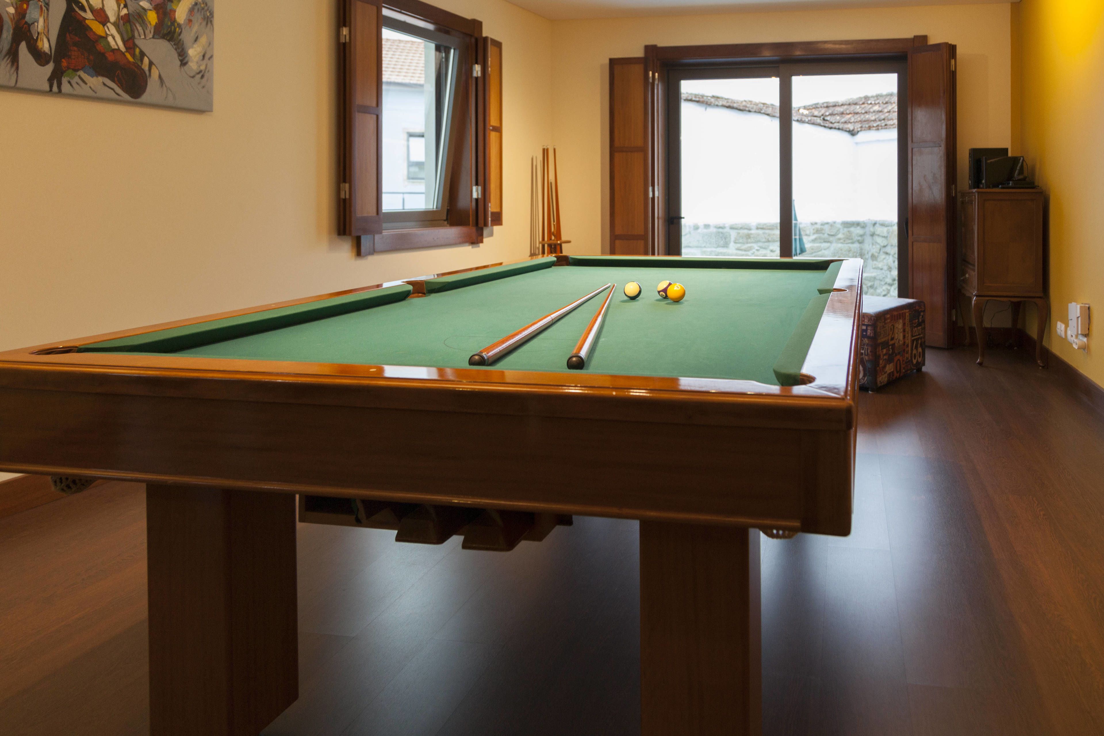 A pool table with cue sticks and balls, a wooden cabinet, and a window with a view.