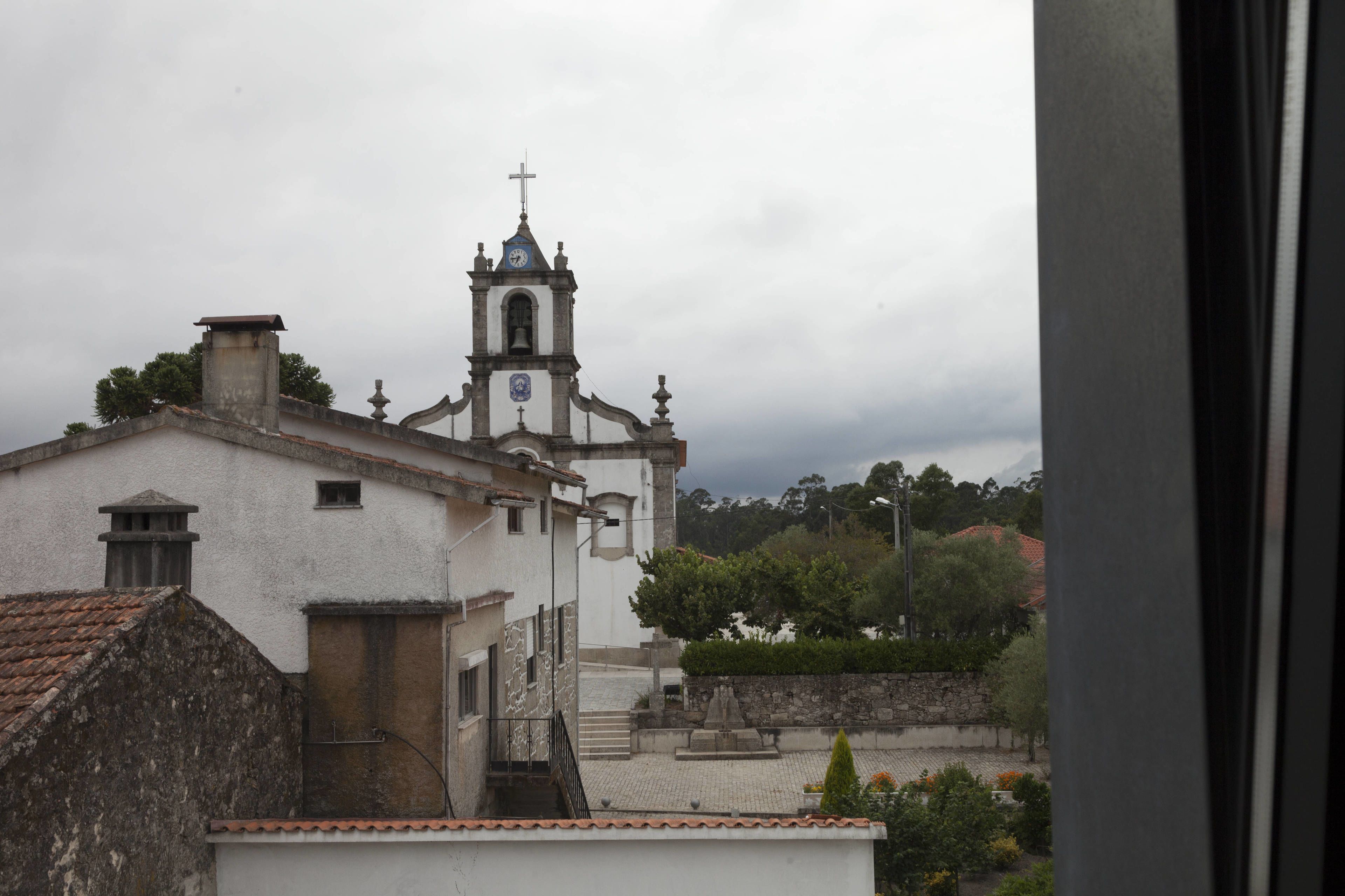 A church with a bell tower and a cross, surrounded by buildings and greenery.