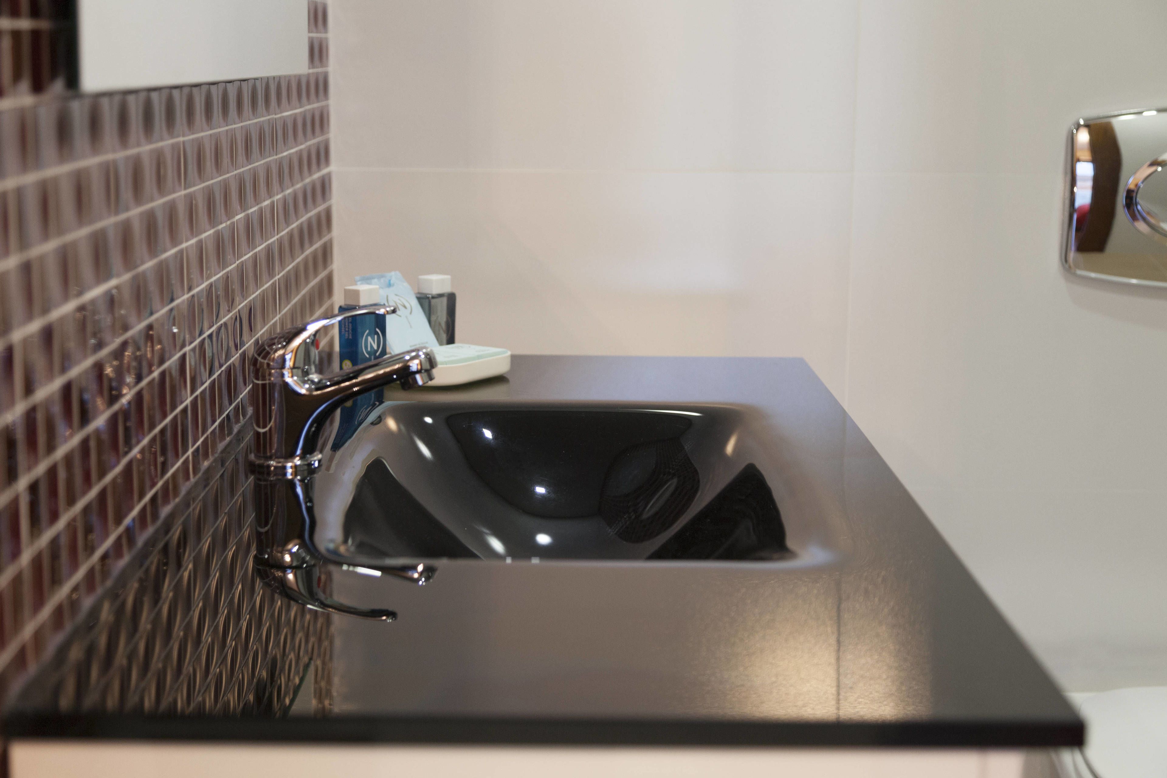 Un baño moderno con un lavabo negro, grifo cromado y salpicadero de azulejos.