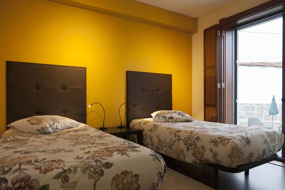 A hotel room with two beds, a wooden headboard, a small table, and a view of the outside.