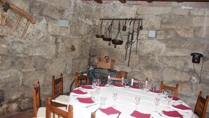 Comedor con paredes de piedra, mesa dispuesta para seis personas, sillas de madera y utensilios de cocina colgando.