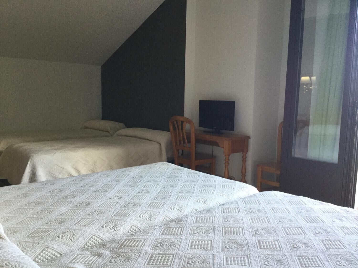 Une chambre avec deux lits, un bureau avec un ordinateur et une fenêtre.