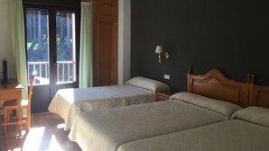 Una habitación con dos camas, un escritorio de madera, una silla, un ventanal con cortinas y una lámpara de pared.