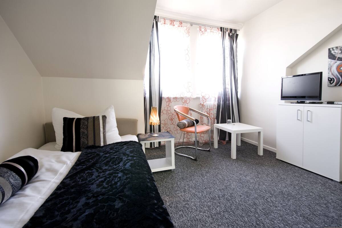 A hotel room with a bed, a desk, a chair, a television, and a window with curtains.